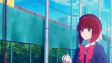 a girl with red hair is standing in front of a fence holding a ball .