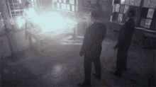 two men are standing in a dark room looking at a fire coming out of a window .