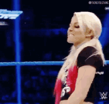 a woman is standing in a wrestling ring with a w logo on the bottom of her shirt .