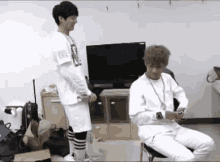 two young men are standing next to each other in a room in front of a tv .