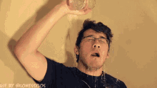 a man with glasses is pouring water from a glass on his face .