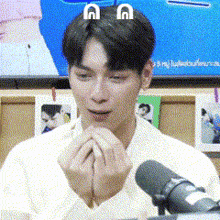 a man is sitting in front of a microphone with his hands folded in front of his face .