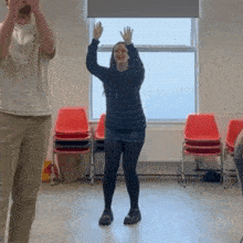 a man and a woman are dancing in a room with red chairs and a window .