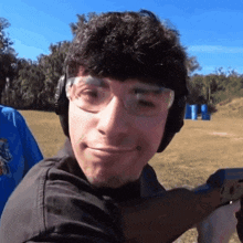 a man wearing headphones and glasses is holding a gun and smiling