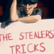 a young man leans on a sign that says the stealers tricks