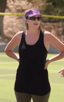 a woman wearing a purple hat and sunglasses stands on a tennis court