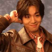 a young man wearing a plaid shirt and a leather jacket