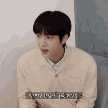 a man wearing a white sweater and a blue shirt has korean writing on the bottom of his face