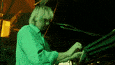 a man in a green shirt playing a keyboard in front of a microphone