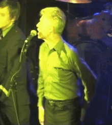 a man in a green shirt singing into a microphone on stage