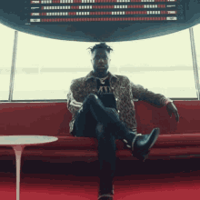 a man sits on a red couch in front of a sign that says " departures "