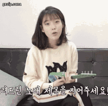 a girl is sitting on a couch holding a green toy guitar with the words gezip.sana written above her