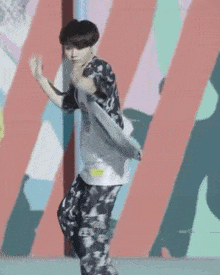 a young man is dancing in front of a colorful wall while wearing a floral shirt and pants .