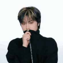 a young man wearing a black sweater is covering his mouth with his hand