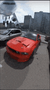 a red mustang is parked in a parking lot with an airplane flying overhead