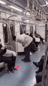 a man is bending over on a subway car while a woman sits on a seat .