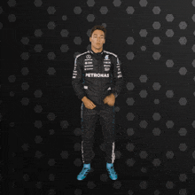 a man wearing a petronas racing suit stands in front of a black background