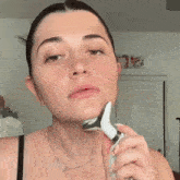 a woman is shaving her face with a razor while wearing a necklace .