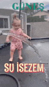 a little girl is playing with water on a trampoline and the words su isezem are on the bottom of the image