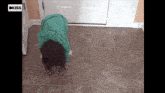 a little girl in a green hoodie is crawling on the floor