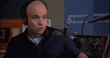a bald man wearing headphones is pointing at something in front of a microphone .