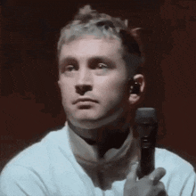 a man in a white shirt is holding a microphone in his hand and making a funny face .