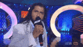 a man in a white suit is holding a microphone that says aew