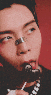 a young man with a bandage on his nose is licking a lollipop