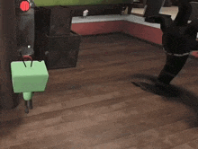 a green cube is sitting on a wooden floor next to a black object