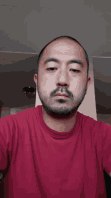 a man with a beard is wearing a red shirt and making a funny face