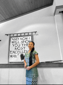 a woman stands in front of a sign that reads " and now i will show you the most excellent way "