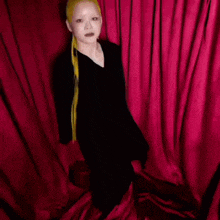 a woman with long blonde hair is standing in front of a red curtain with the words coco n on the bottom