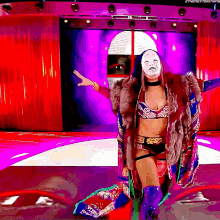 a woman wearing a fur coat and a mask stands in front of a screen that says thenextthing