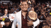 a man holding a wrestling championship belt in front of a crowd of people