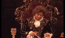 a man in a black and gold costume is sitting in a red chair