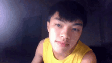 a young asian man wearing a yellow tank top looks at the camera