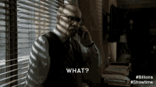 a man in a suit and tie is talking on a cell phone while standing in front of a window with blinds ..