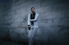 a man in a white suit stands in front of a brick wall with his arms crossed