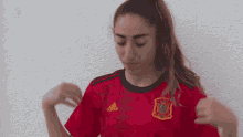 a woman wearing a red adidas shirt stands in front of a white wall