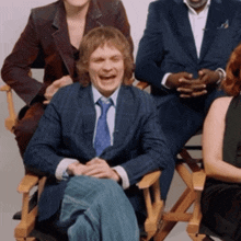 a man in a suit and tie is laughing while sitting in a directors chair
