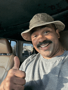 a man wearing a hat gives a thumbs up in a car