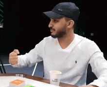 a man wearing a hat and a white sweater is sitting at a table .