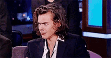 a man in a suit is sitting in a chair and making a face .