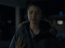 a woman wearing a jacket with a fur hood smiles in the dark