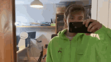 a man in a green hoodie is taking a selfie with a cell phone .