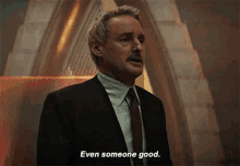 a man in a suit and tie is standing in front of a building and says `` even someone good . ''