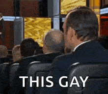 a man in a suit is sitting in a row of seats with the words `` this gay '' written on it .