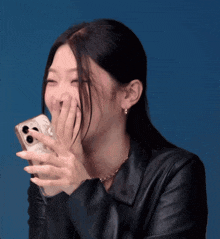 a woman in a leather jacket is laughing while holding a phone