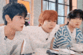 three young men are sitting at a table with cups of coffee and plates of food .