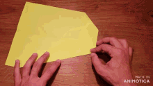 a person holding a piece of yellow paper with the words made in animotica on the bottom right